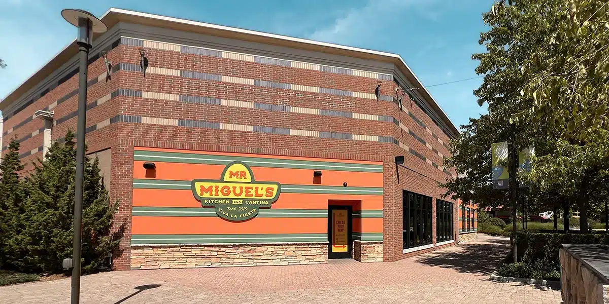 Exterior view of Mr. Miguel's Kitchen and Cantina, featuring a colorful sign and brick facade, surrounded by greenery.