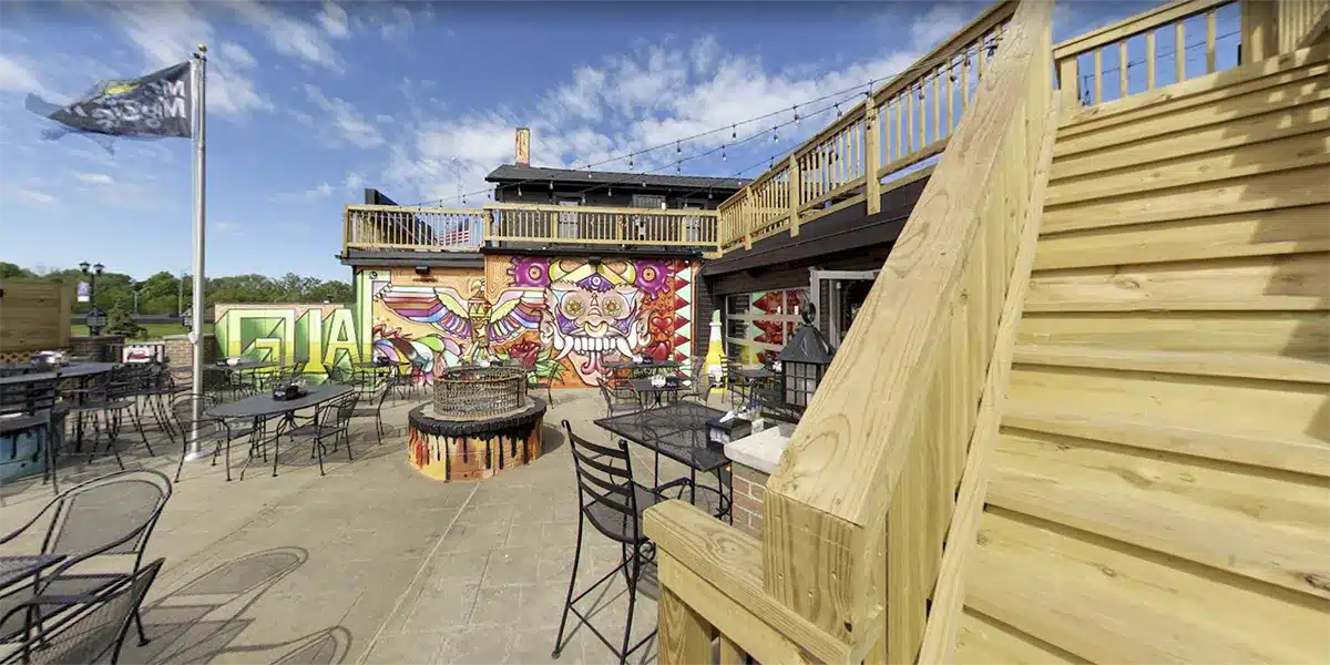 vibrant outdoor dining area features colorful murals, tables, and a staircase leading to an upper deck.